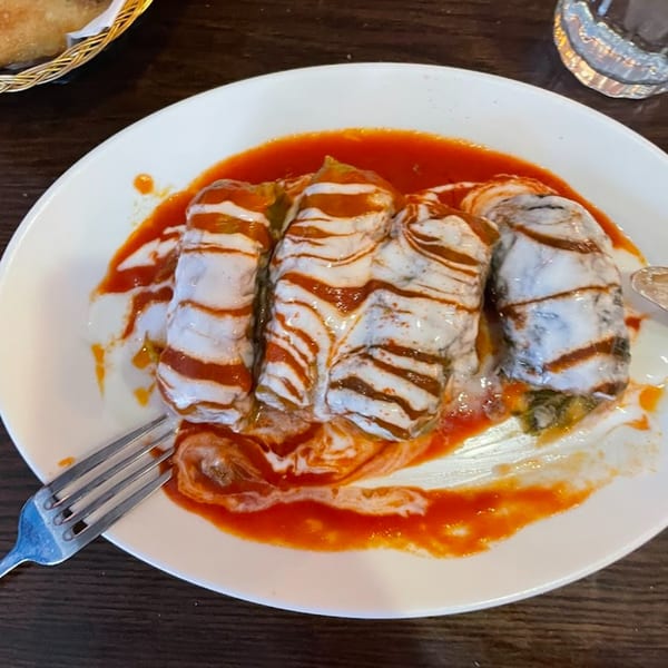 Turkish stuffed cabbage rolls with yogurt and tomato sauce on a white plate with a fork.