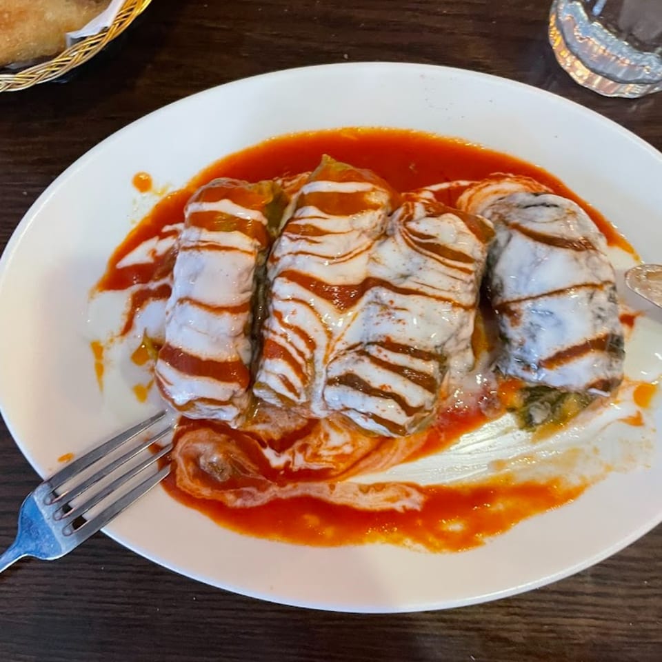 Turkish stuffed cabbage rolls with yogurt and tomato sauce on a white plate with a fork.