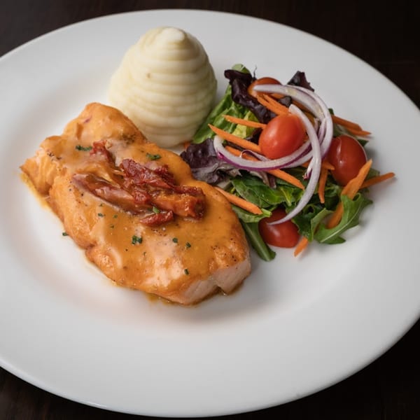 Salmon with creamy sauce and sun-dried tomatoes, served with mashed potatoes and a side salad.