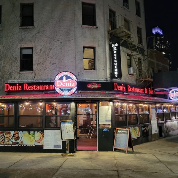 Exterior of Deniz Turkish Restaurant at night, with bright red neon signs and illuminated windows.