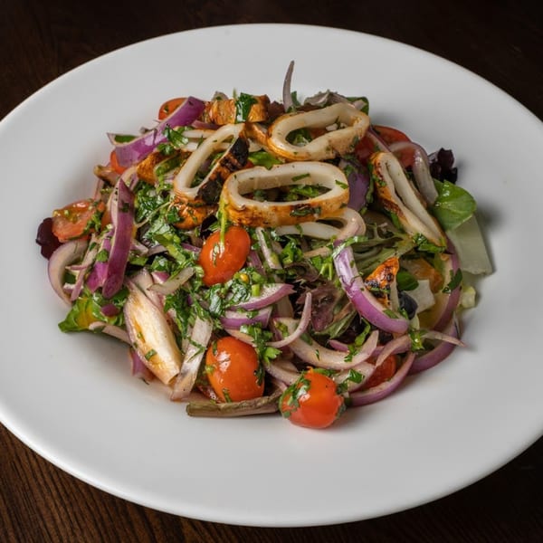 Grilled calamari salad with red onions, cherry tomatoes, and fresh herbs on a white plate.