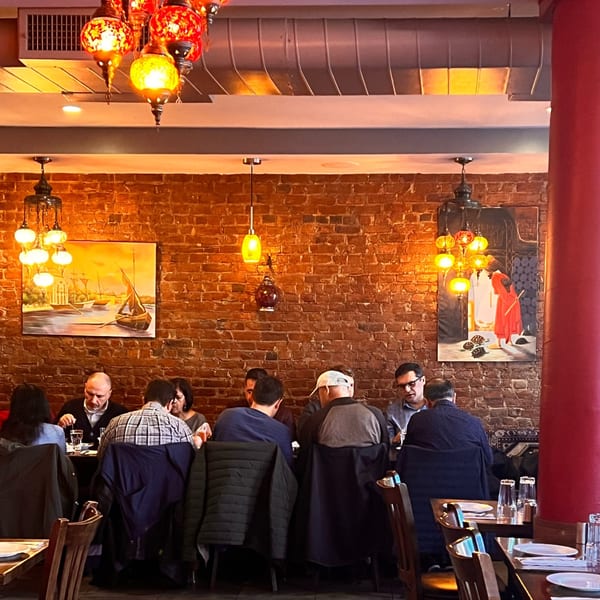 Diners seated at tables in Deniz Mediterranean Turkish Cuisine, with brick walls and ornate Turkish lamps.