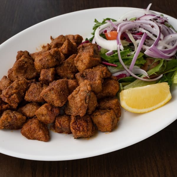 Turkish fried liver cubes, Arnavut Ciğeri, with a side salad of greens, red onion, and a lemon wedge.