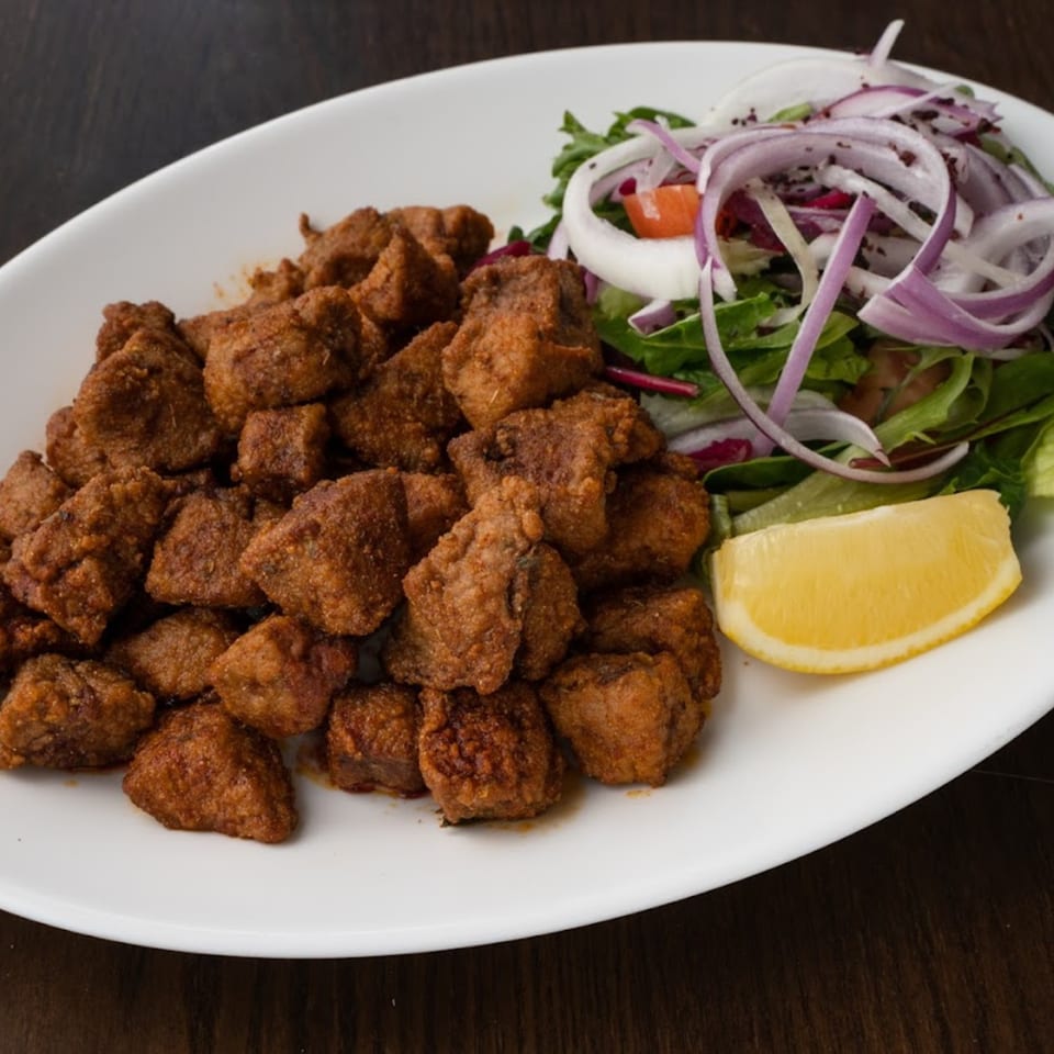 Turkish fried liver cubes, Arnavut Ciğeri, with a side salad of greens, red onion, and a lemon wedge.