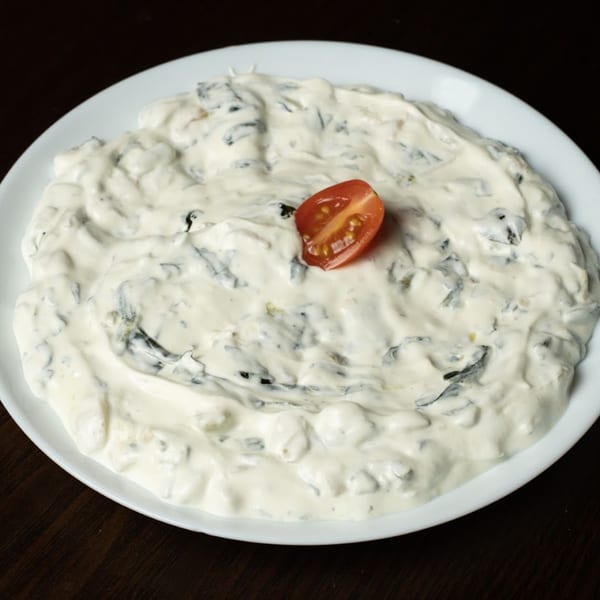 Creamy Turkish spinach dip with a cherry tomato garnish on a white plate.