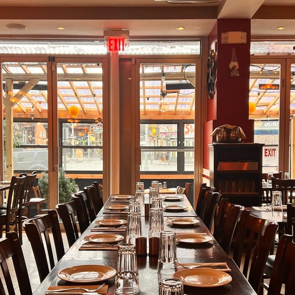Long dining table set with plates and glasses, facing large windows in Deniz Mediterranean Turkish Cuisine.