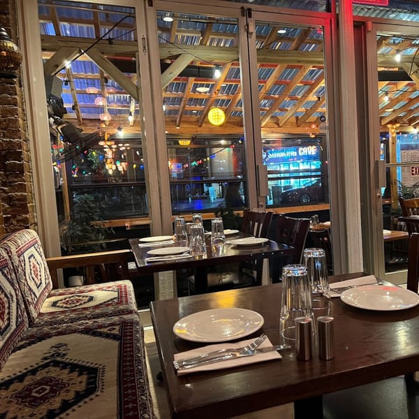 Interior of Deniz Turkish Cuisine with set tables, patterned banquette, and large windows looking out to the street.