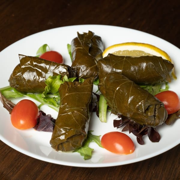 Turkish dolmas, grape leaves stuffed with rice, served with cherry tomatoes and a lemon slice.