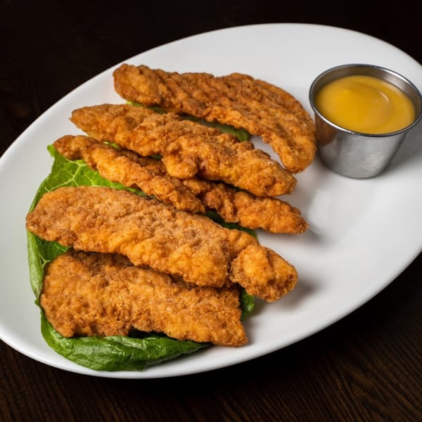 Crispy fried chicken tenders on a bed of lettuce with a side of honey mustard sauce.