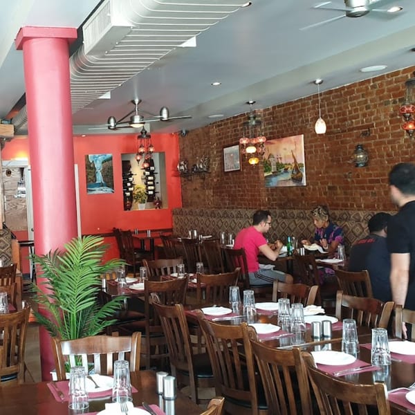 Deniz Mediterranean Turkish Cuisine dining room with brick walls, red accents, and patrons enjoying meals.